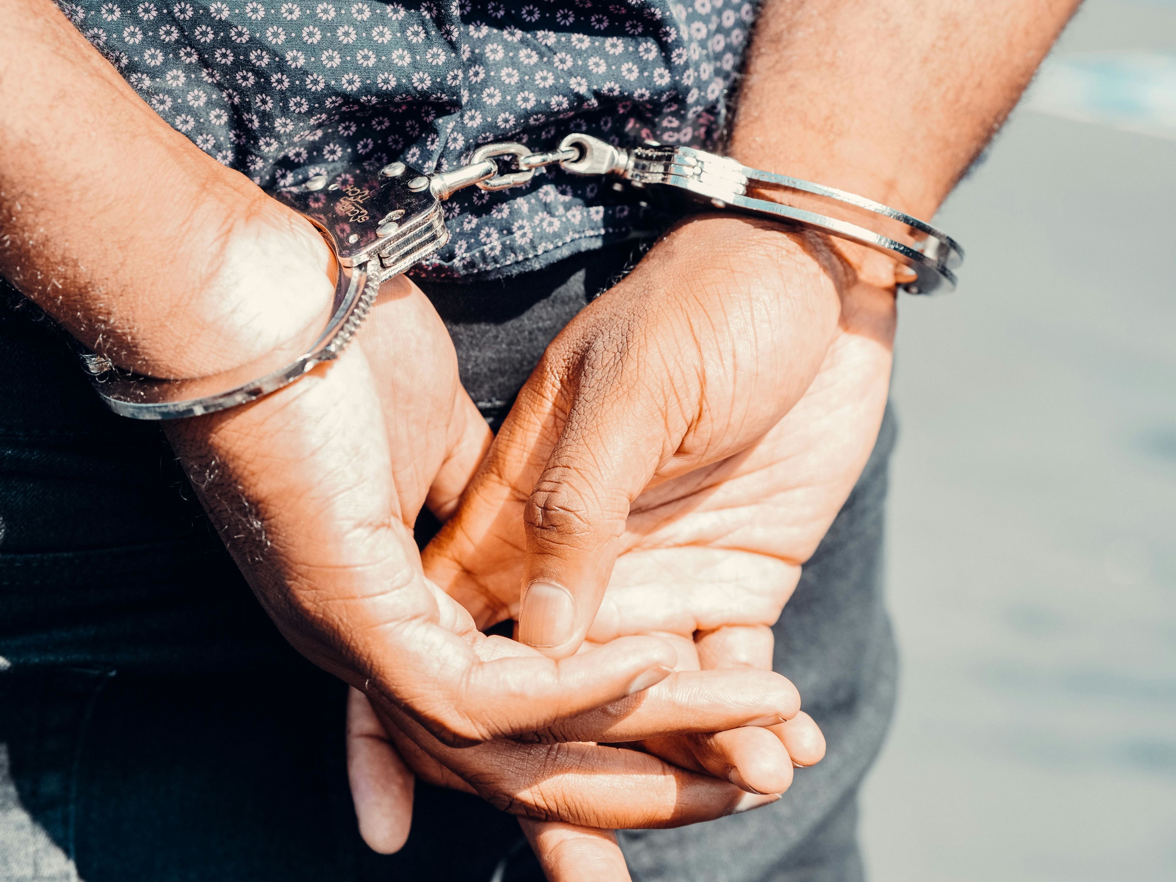 Close-up of an adult male's hands in handcuffs, symbolizing law enforcement and justice.