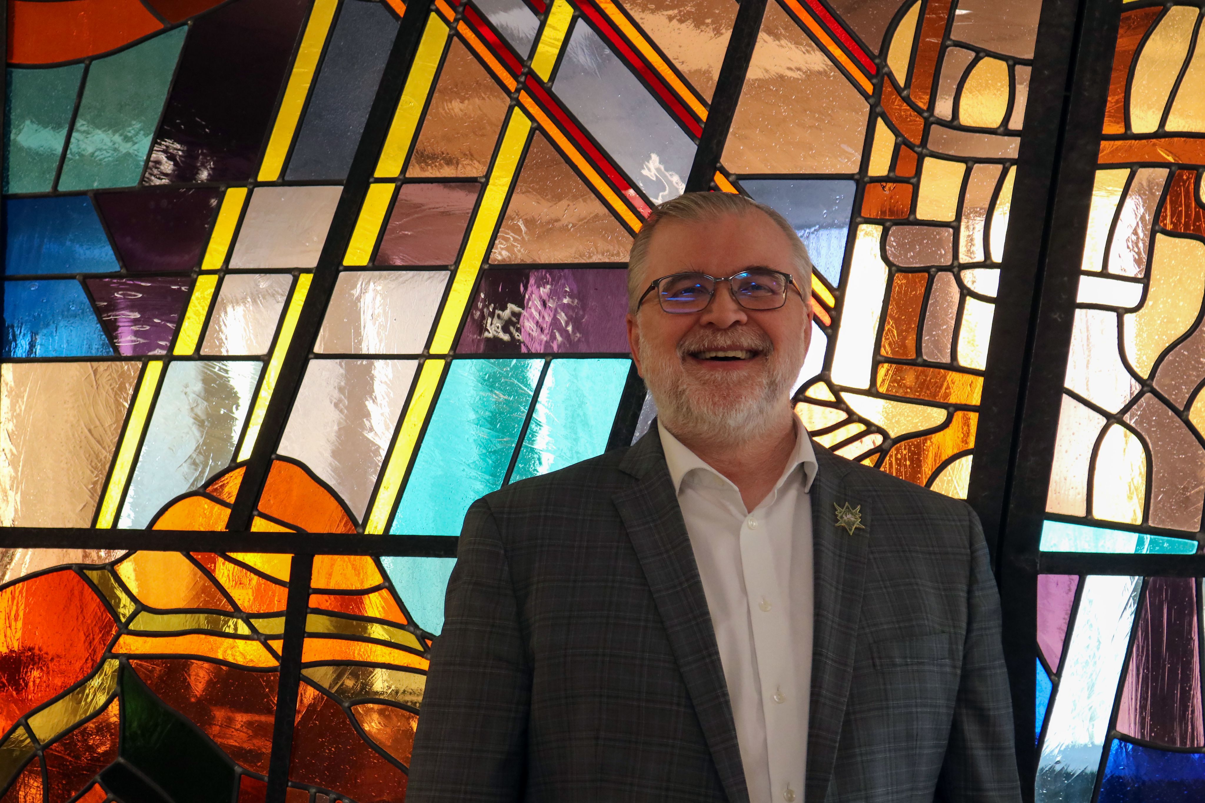 Rabbi Russell Jayne stands in front of a stained glass window in Beth Tzedec Congregation. 